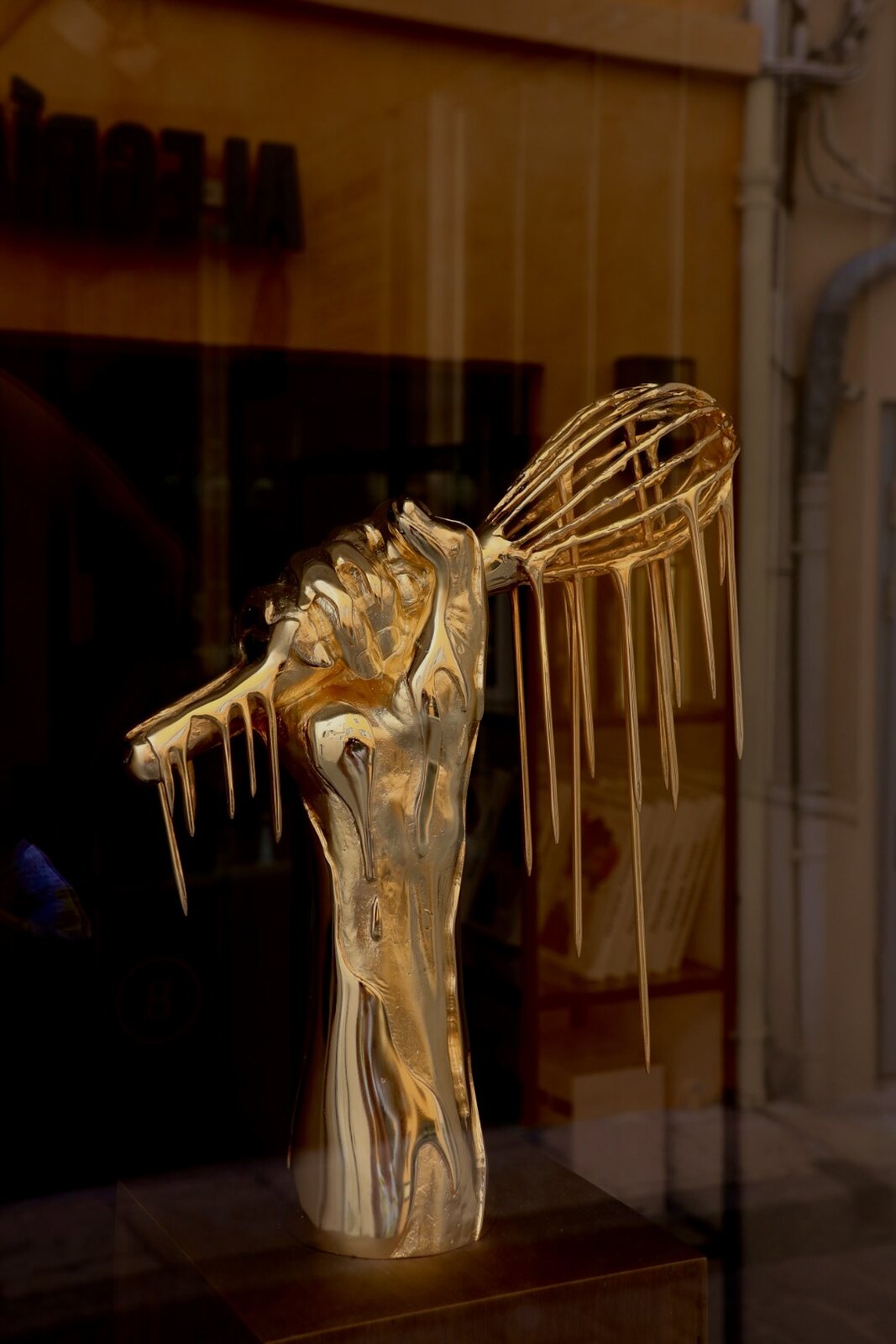 Goldene Skulptur einer Hand mit tropfendem Schneebesen im Schaufenster
