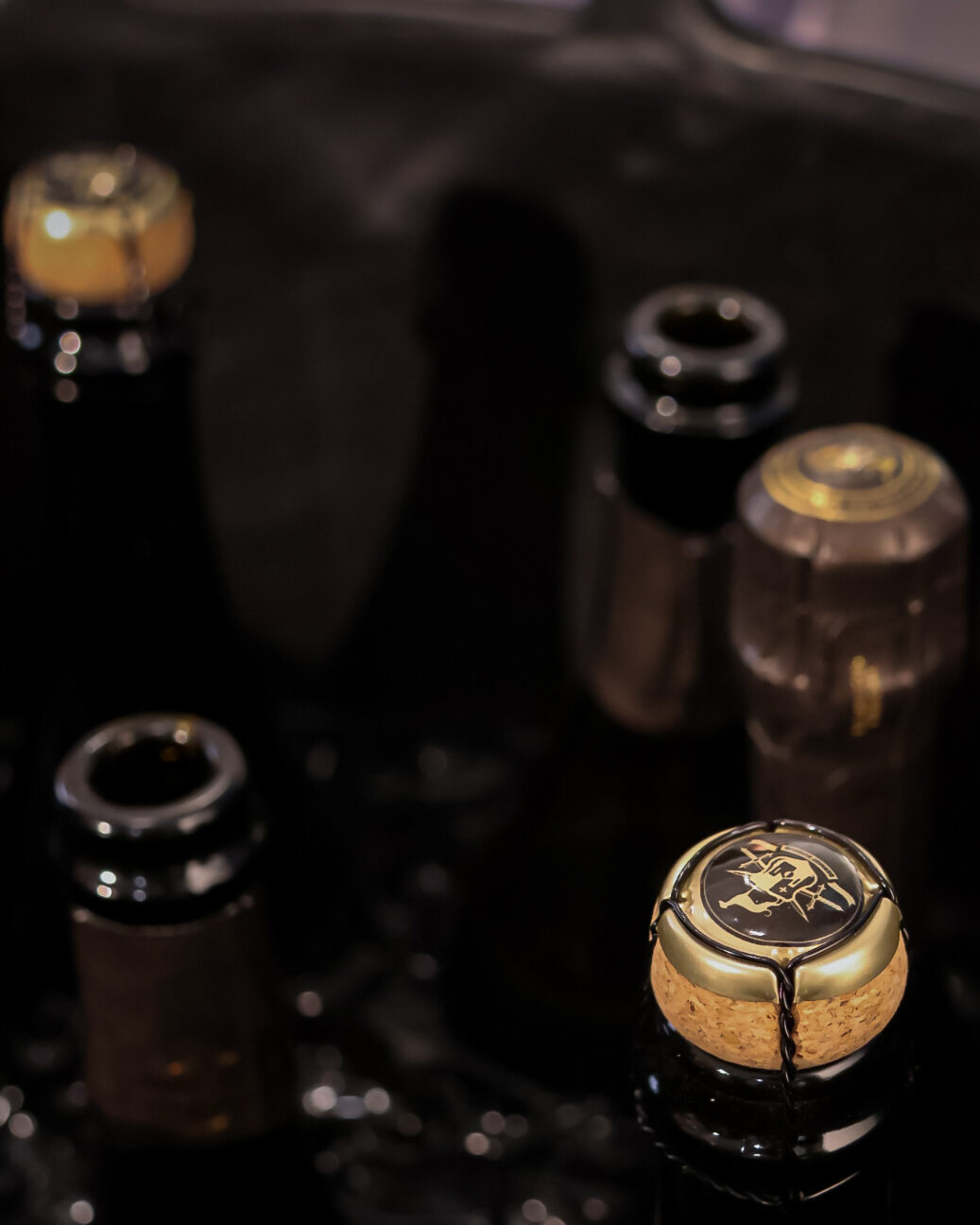 Champagnerkorken mit goldener Agraffe und offene Flaschenhälse im dunklen Kühler