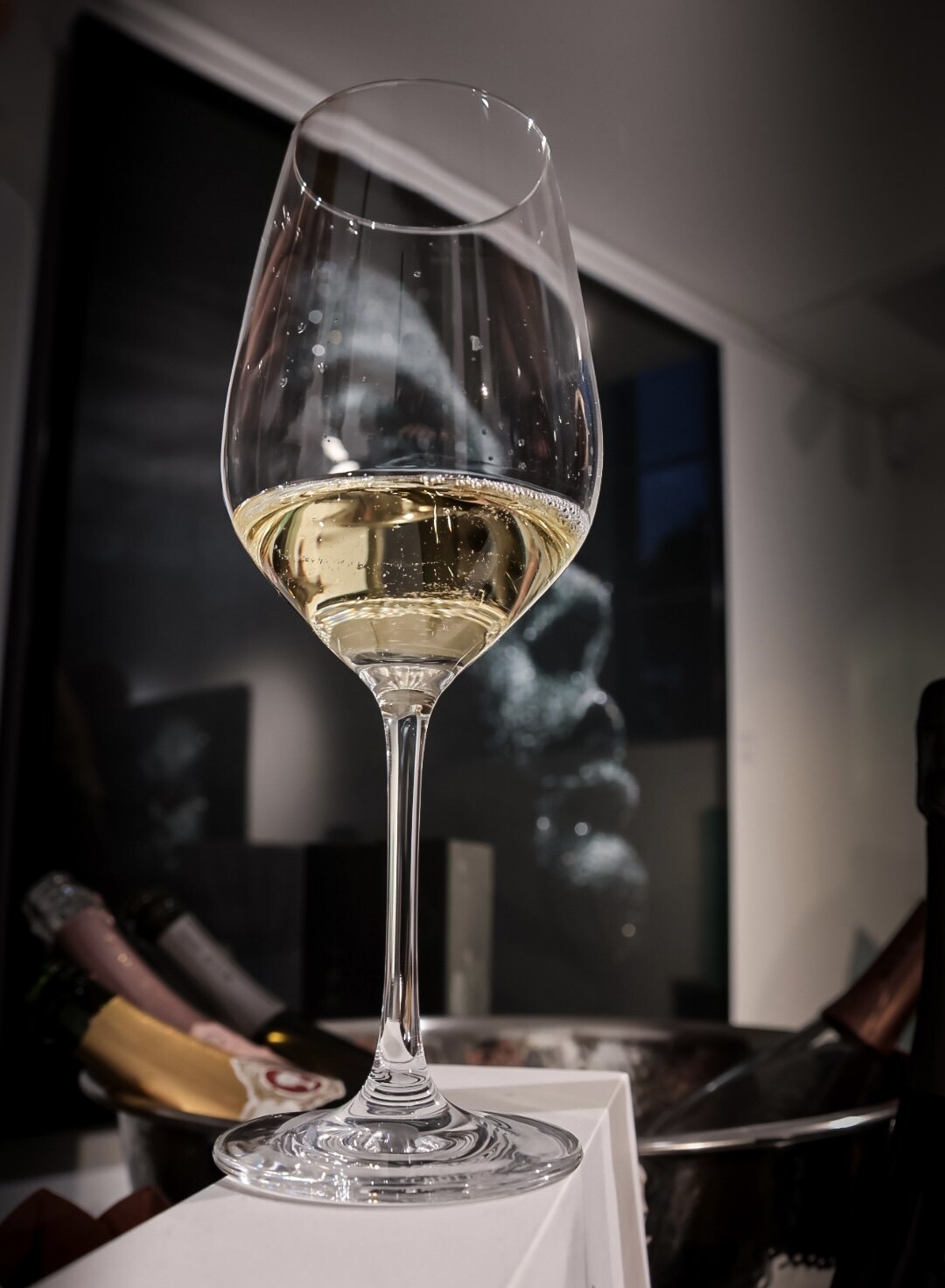 Glas Champagner mit aufsteigender Perlage vor einem dunklen Kunstwerk