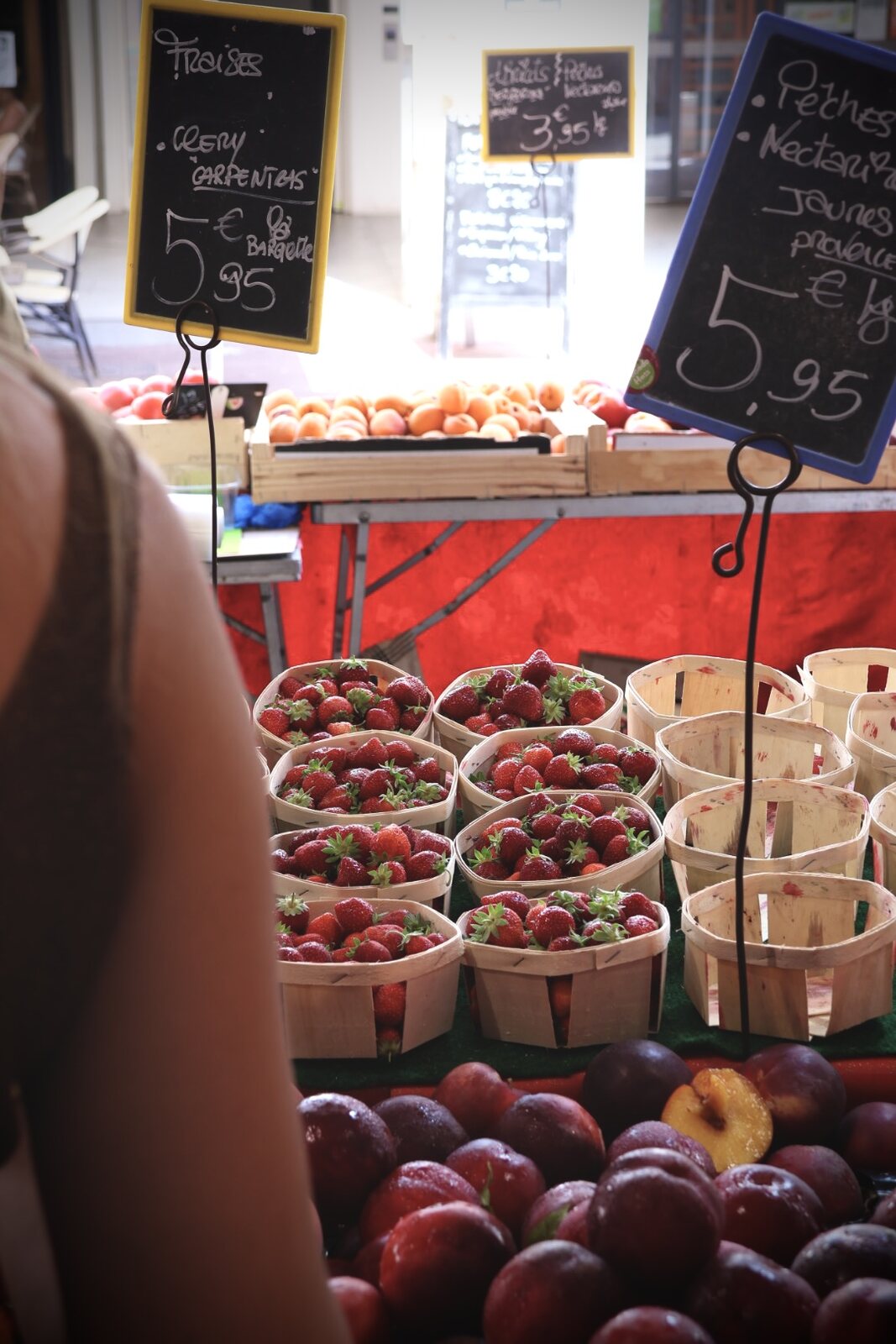 Erdbeerkörbchen und Pfirsiche mit Kreidetafeln an einem Marktstand