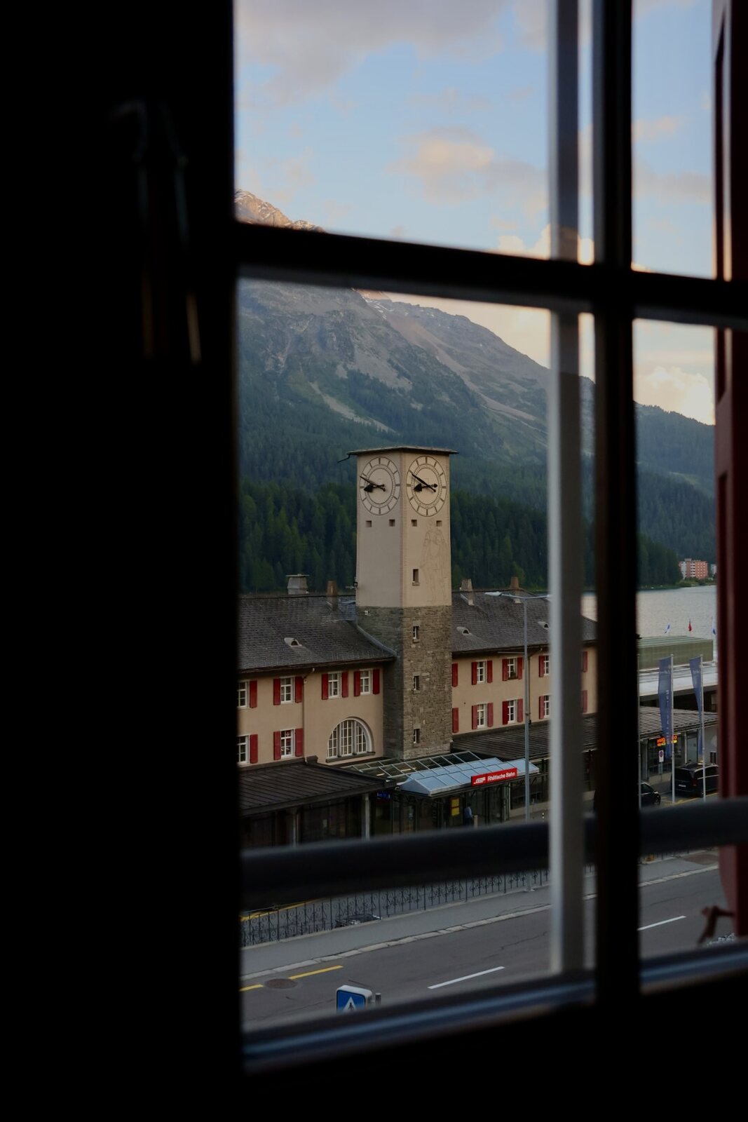 Durch ein Sprossenfenster: Bahnhof St. Moritz mit Uhrturm, See und Berge