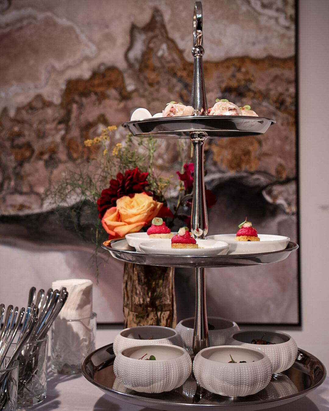 Silberne Etagere mit Randen-Tartelettes und Porzellanschalen vor einem Gemälde