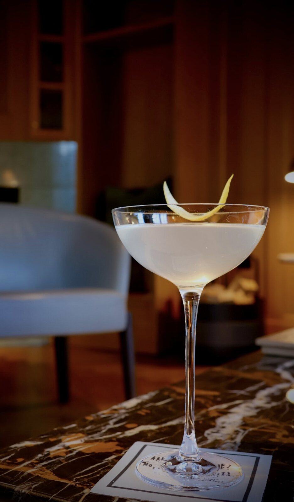 Cocktail in einer Coupe mit Zitronenzeste auf Marmor in einer Hotelbar