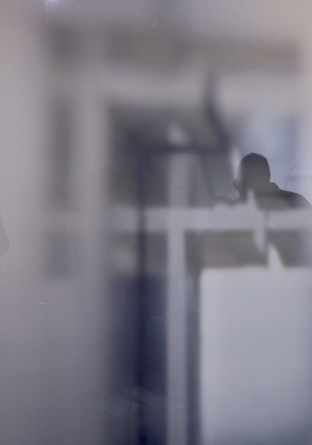 Silhouette eines Mannes hinter einer matten Glasscheibe, weiche Grautöne und Fensterkreuz
